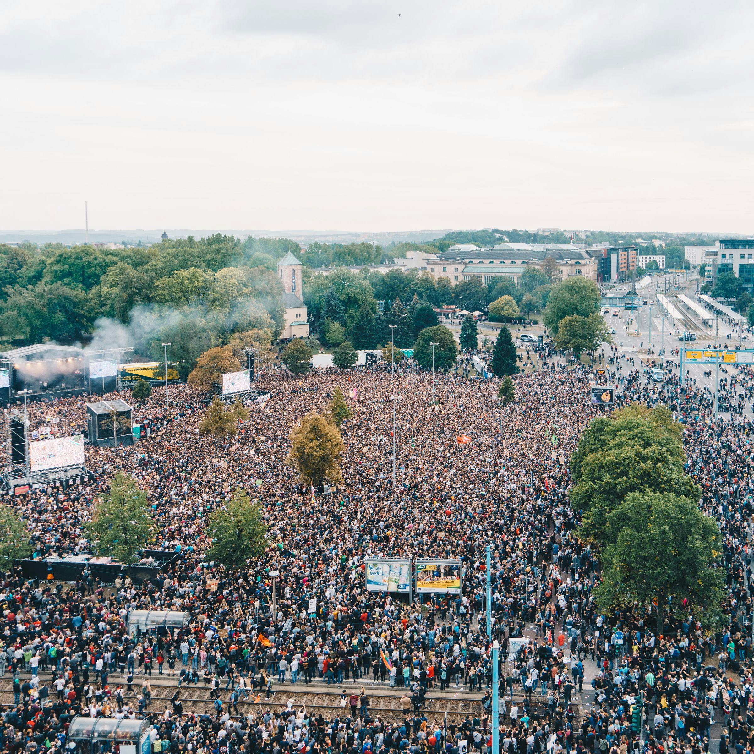Man sieht ein Foto vom KOSMOS 2018, ber der eine Menschenmenge (von oben fotografiert) den Platz vor der Bühne komplett füllt. Die Straßen daneben sind auch von Menschen gefüllt.